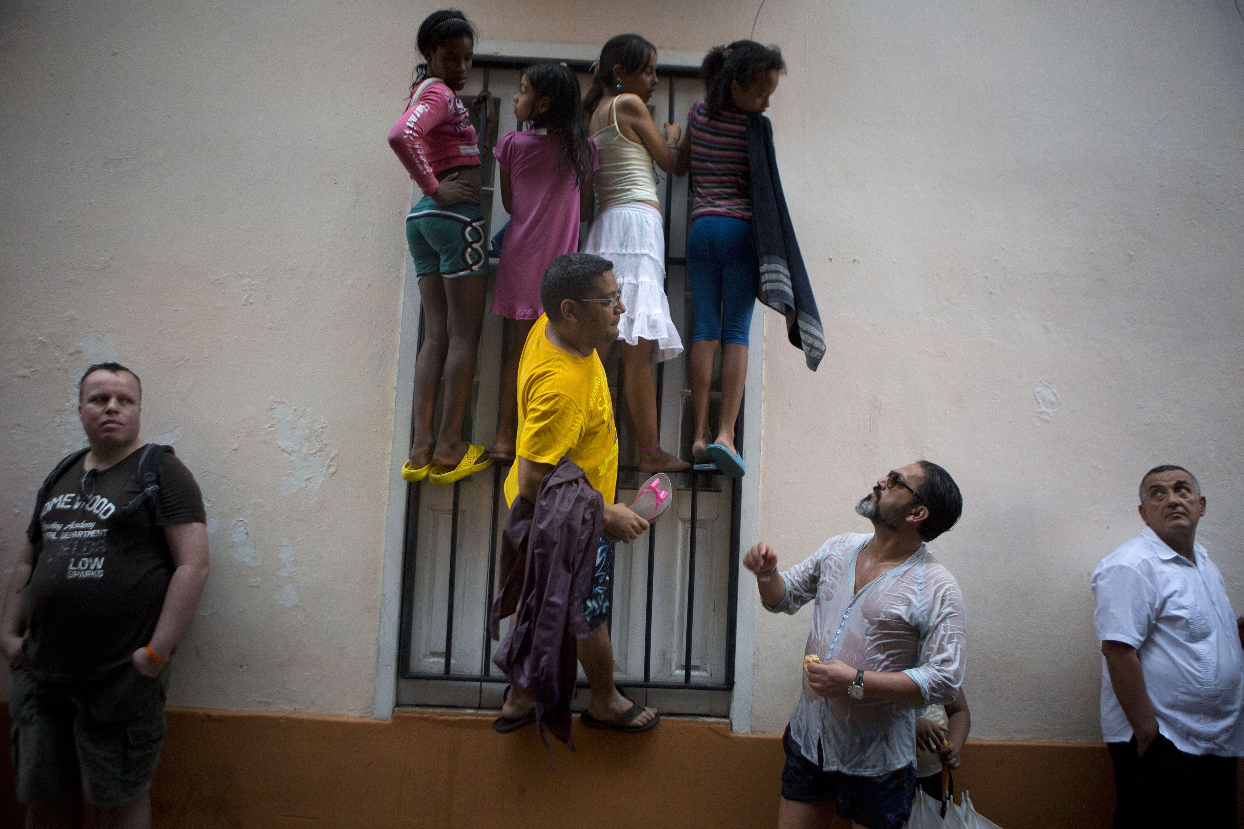 People climb a window grate as they get wet in the rain, in hopes of catching a glimpse of President Barack Obama during his visit to Cathedral Square in Old Havana, Cuba, Sunday, March 20, 2016. Obama's trip is a crowning moment in his and Cuban President Raul Castro's ambitious effort to restore normal relations between their countries. (AP Photo/Rebecca Blackwell)